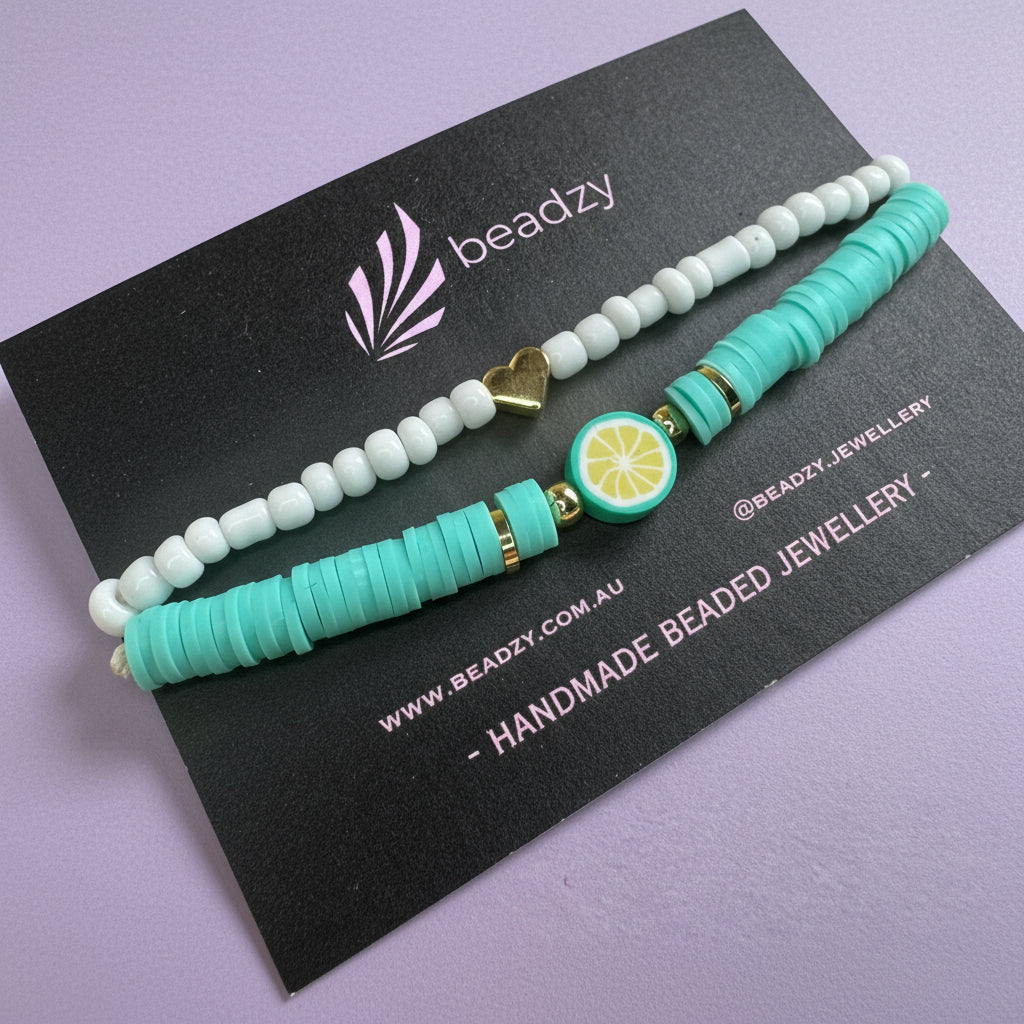 Turquoise beaded hair tie with lemon charm on a black card with brand name on a yellow background - Beadzy