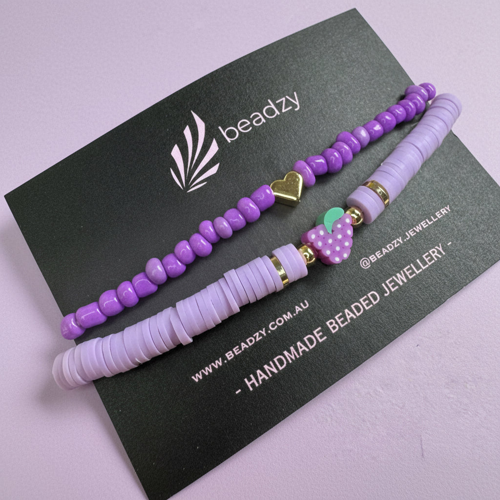 Purple beaded hair ties on a black card with 'beadzy' branding against a yellow background - Beadzy