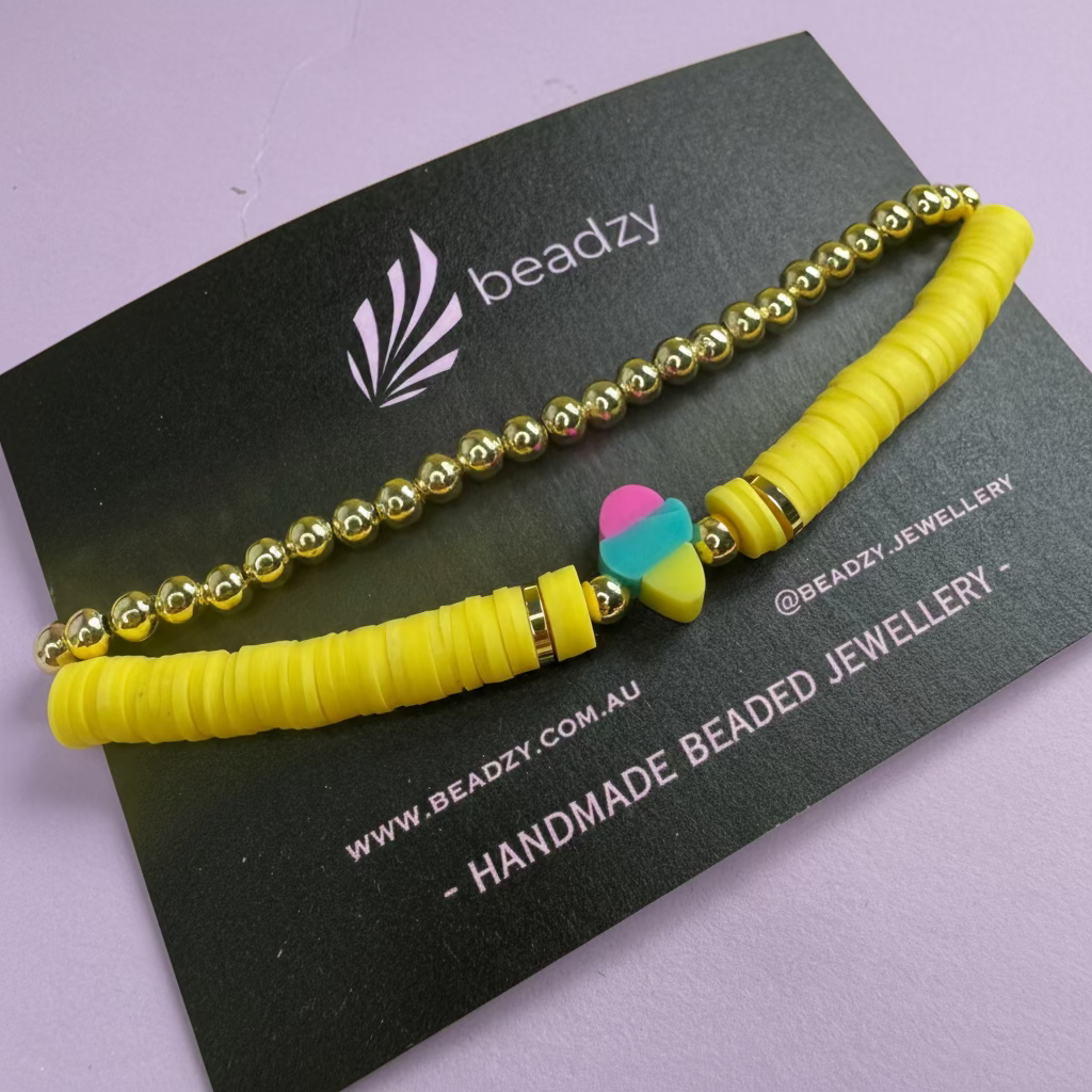 Yellow beaded bracelet with a heart charm on a black card with 'beadzy' branding. - Beadzy