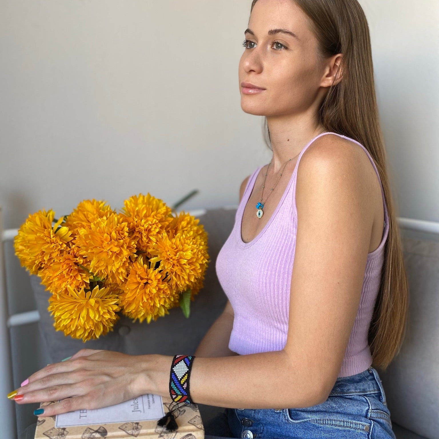 Woman holding a bouquet of yellow flowers and a book, sitting on a couch.