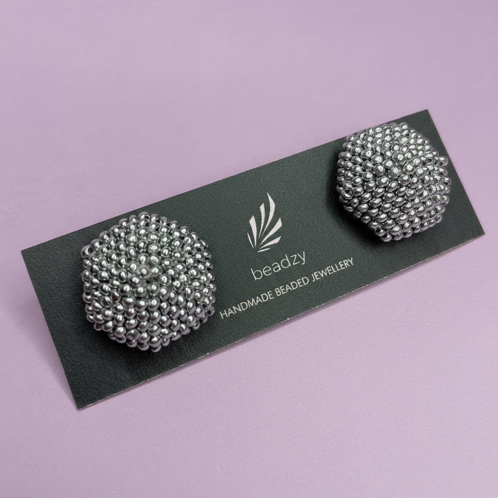 Pair of silver beaded earrings on a black card with 'beadzy' branding against a light purple background. - Beadzy