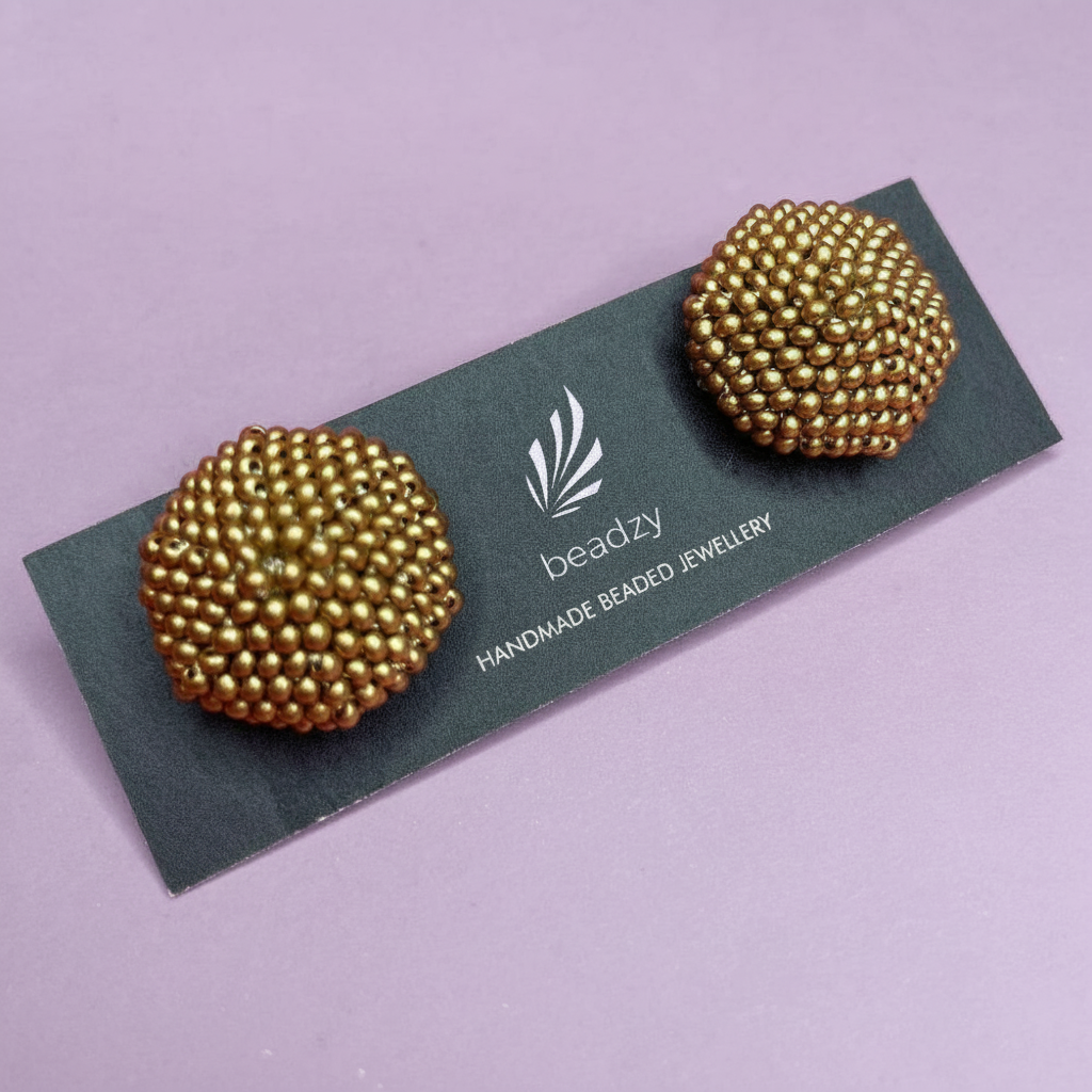 Gold beaded earrings on a 'beadzy' branded card against a purple background - Beadzy
