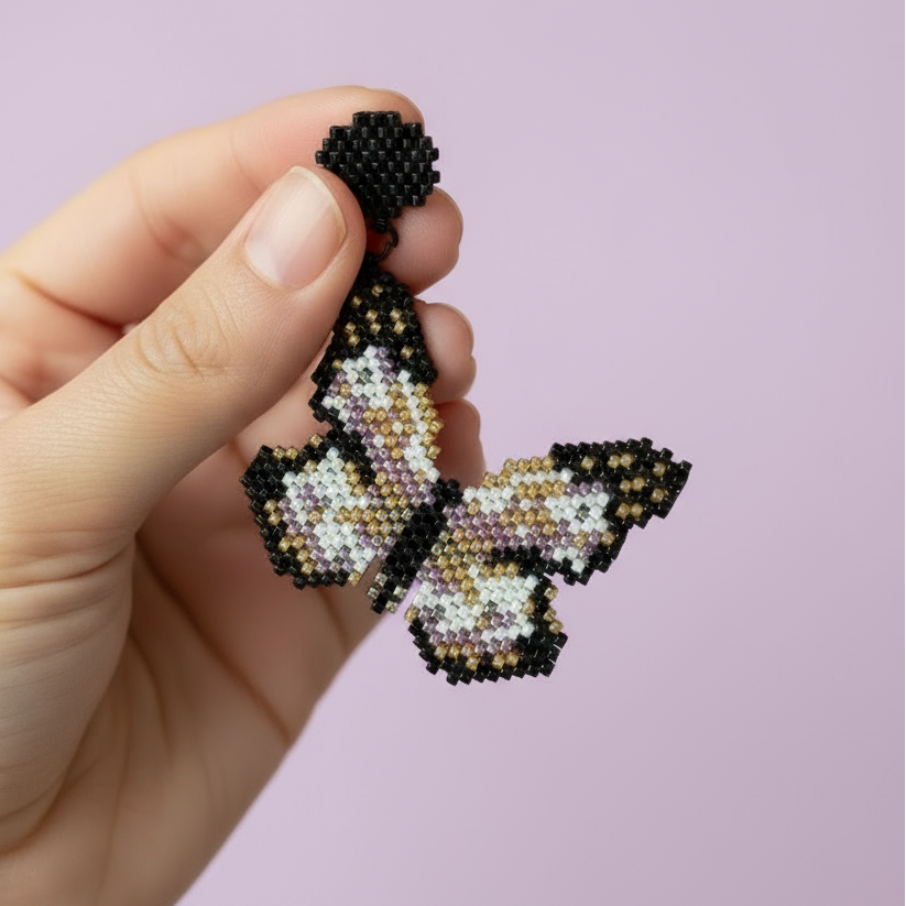 Hand holding a beaded butterfly earrings against a purple background - Beadzy