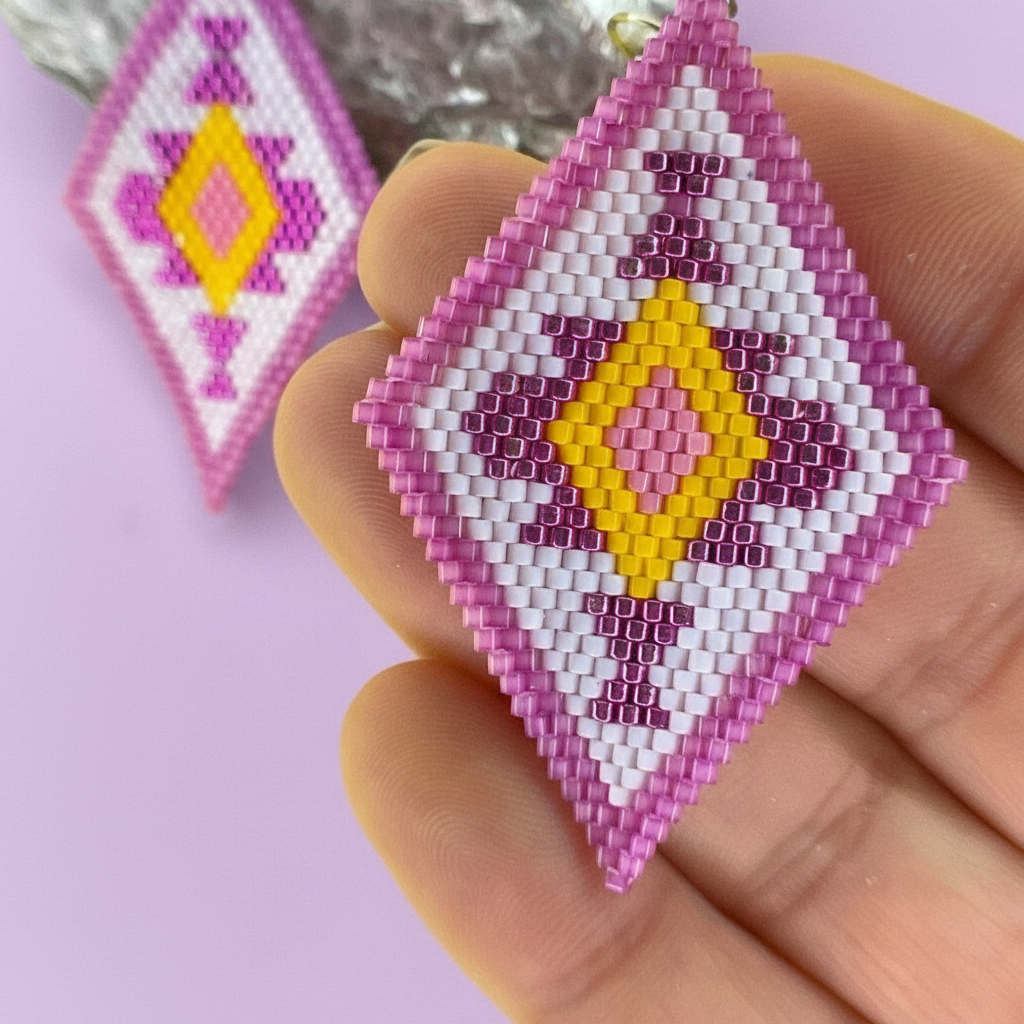 Hand holding a beaded earring with pink, yellow, and white pattern on a light purple background - Beadzy