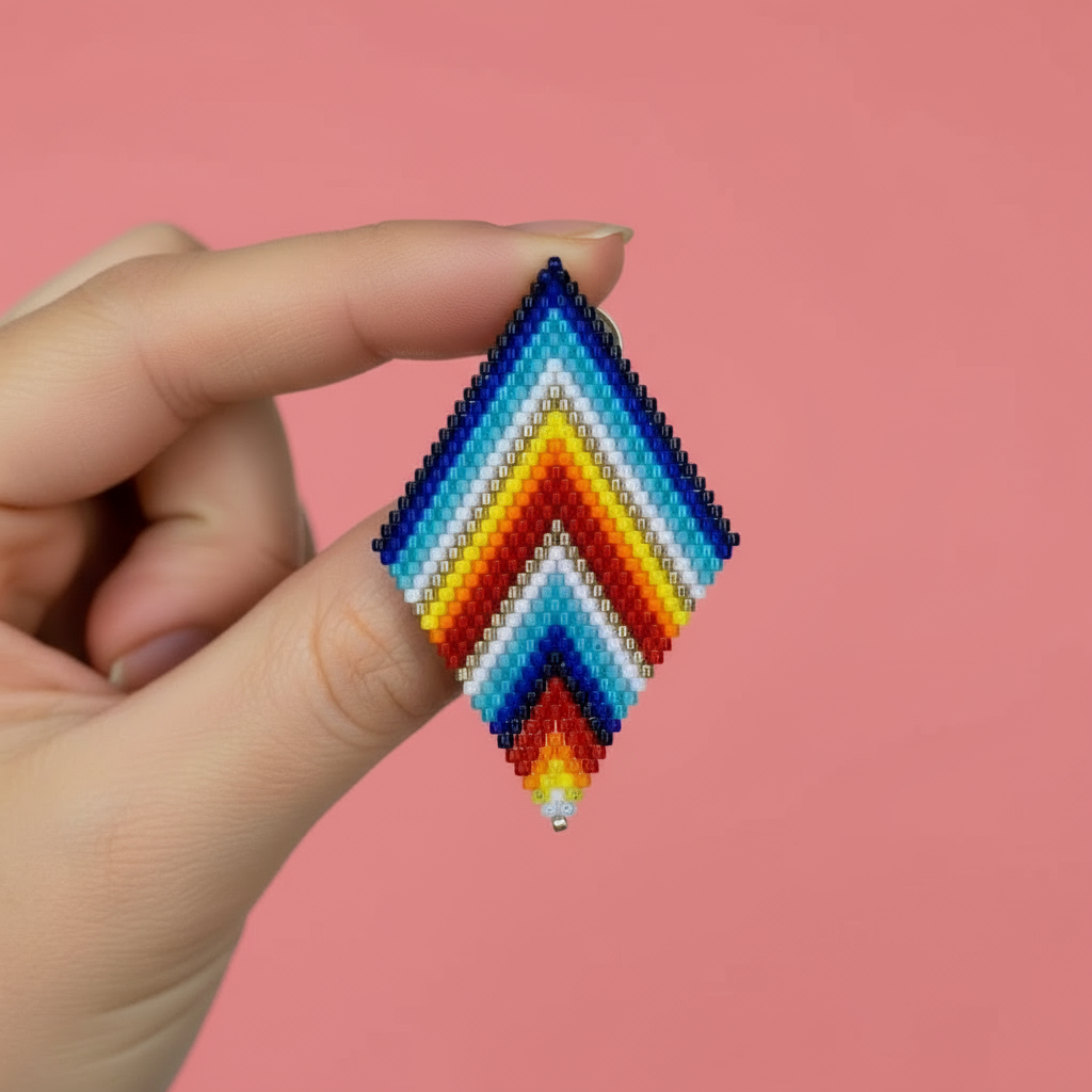 Hand holding a rainbow color beaded diamond shape earrings against a pink background - Beadzy