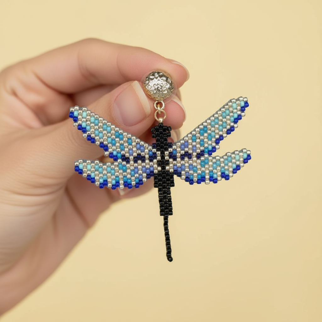 Hand holding a beaded dragonfly earrings against a yellow background - Beadzy