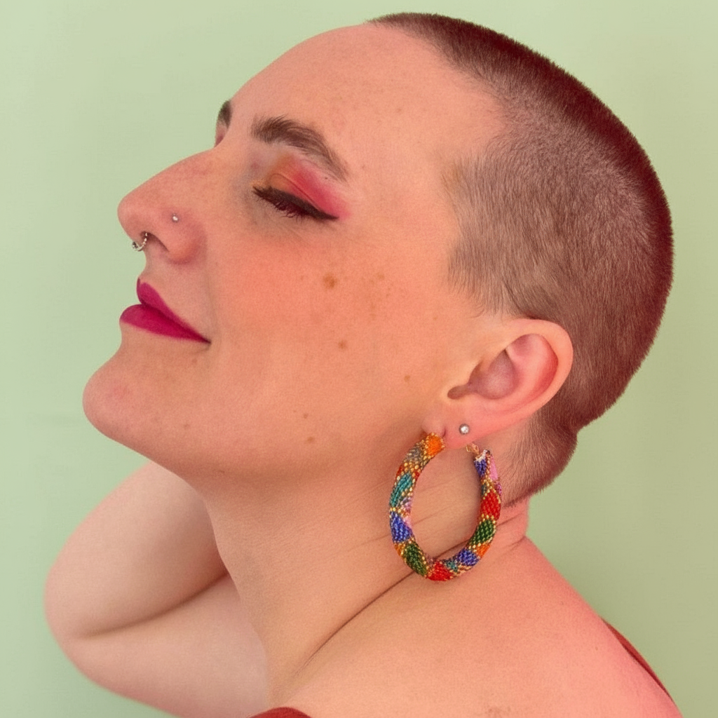 Person wearing colorful hoop earrings against a light green background - Beadzy