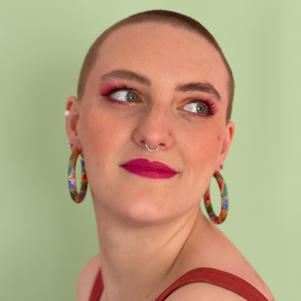 Person with shaved head wearing colorful hoop earrings and red lipstick on a light green background - Beadzy