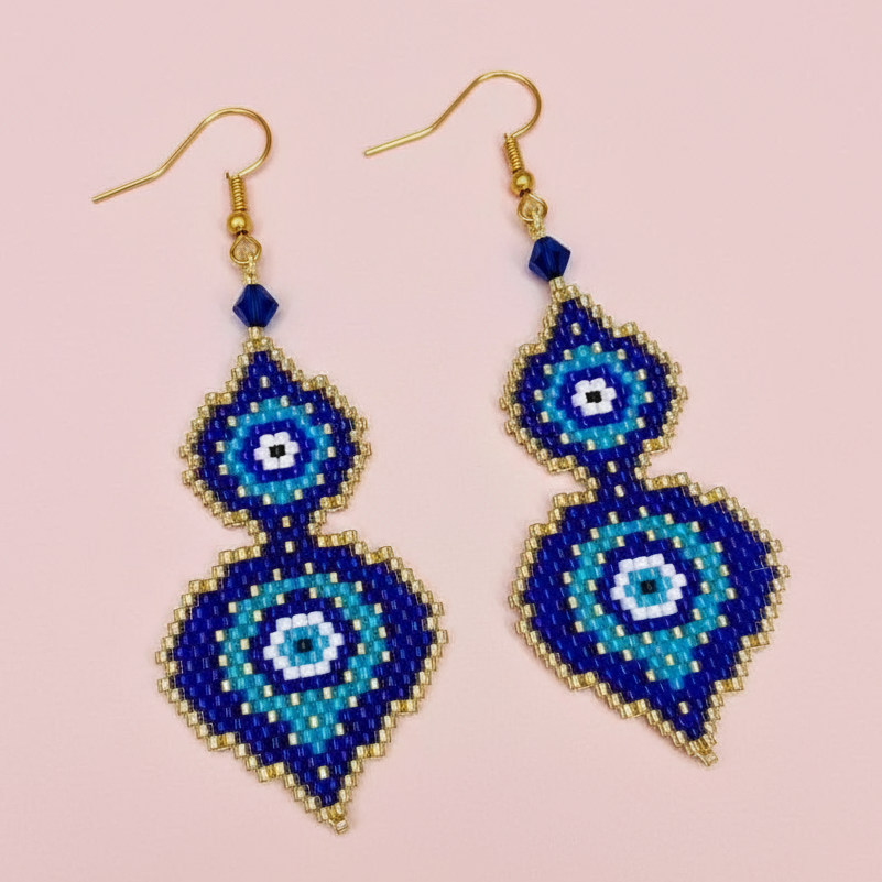 Blue evil eye beaded earrings with gold accents on a pink background - Beadzy