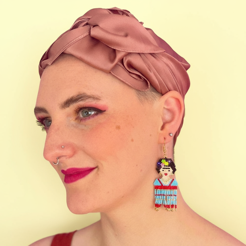 Woman wearing a pink headscarf and colorful Frida earrings on a yellow background - Beadzy