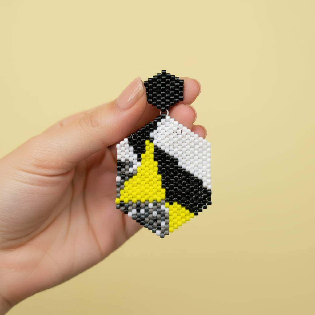 Hand holding a pair of beaded earrings with black, white, and yellow design on a beige background - Beadzy
