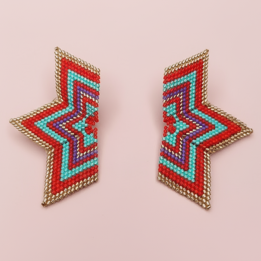 Star-shaped red and gold beaded earrings on a pink background - Beadzy