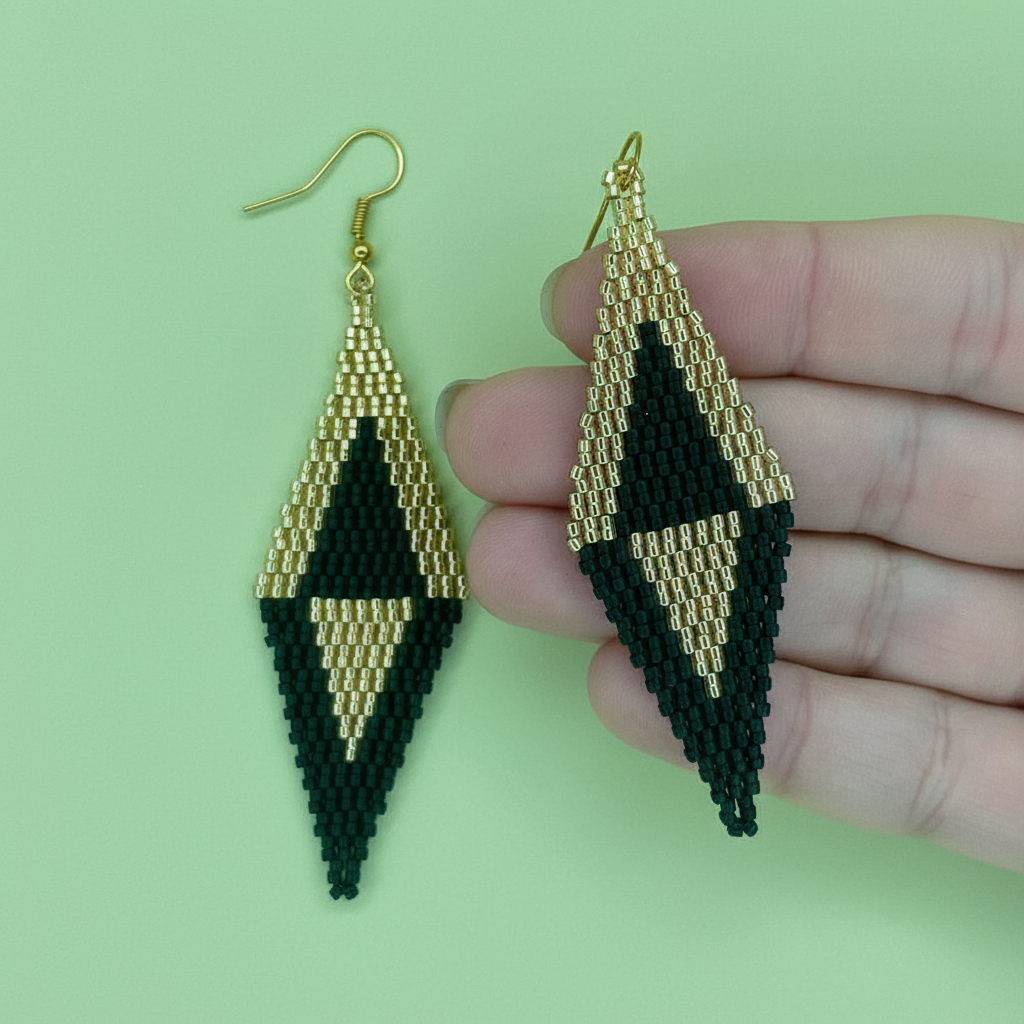 Black and gold beaded earrings held by a hand against a green background - Beadzy