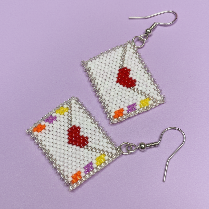Beaded earrings with envelope shape heart designs on a purple background - Beadzy