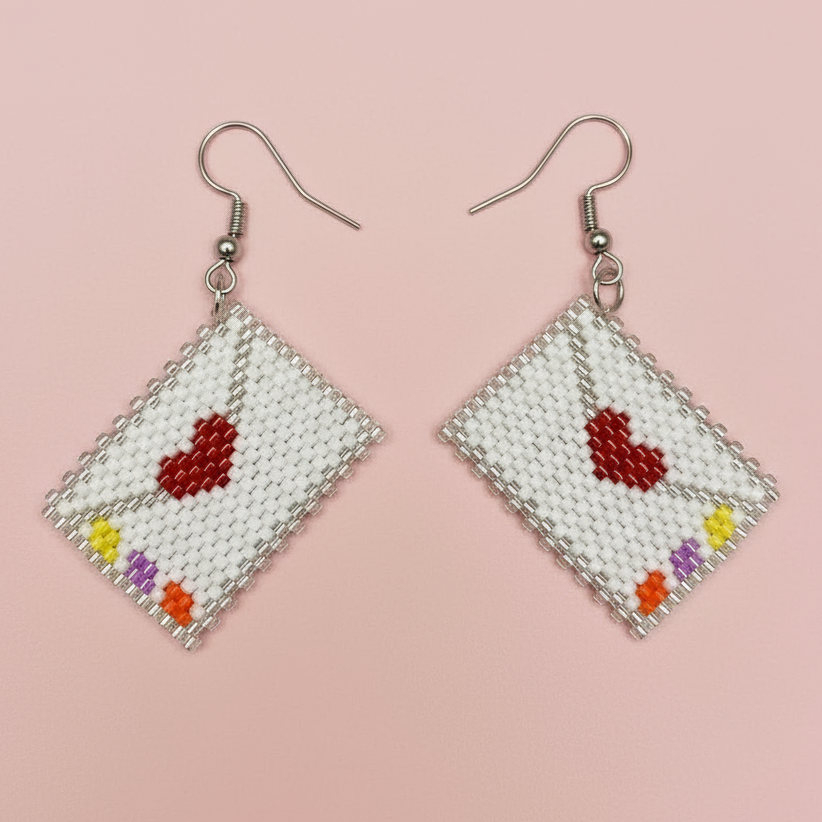 Envelope shaped beaded earrings with red hearts and colorful beads on a pink background - Beadzy