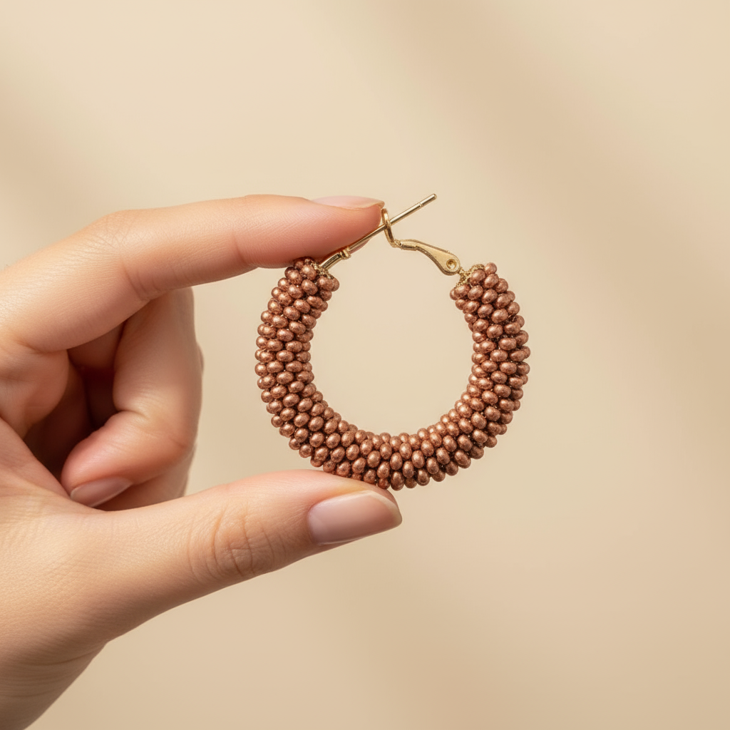 Hand holding a beaded hoop earring against a beige background - Beadzy