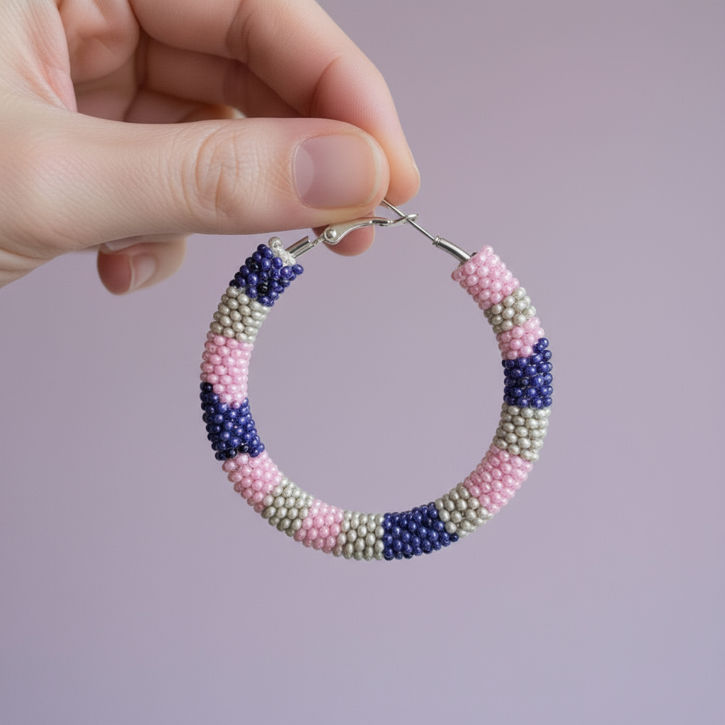 Hand holding a beaded hoop earring with pink, blue, and beige colors on a light purple background - Beadzy