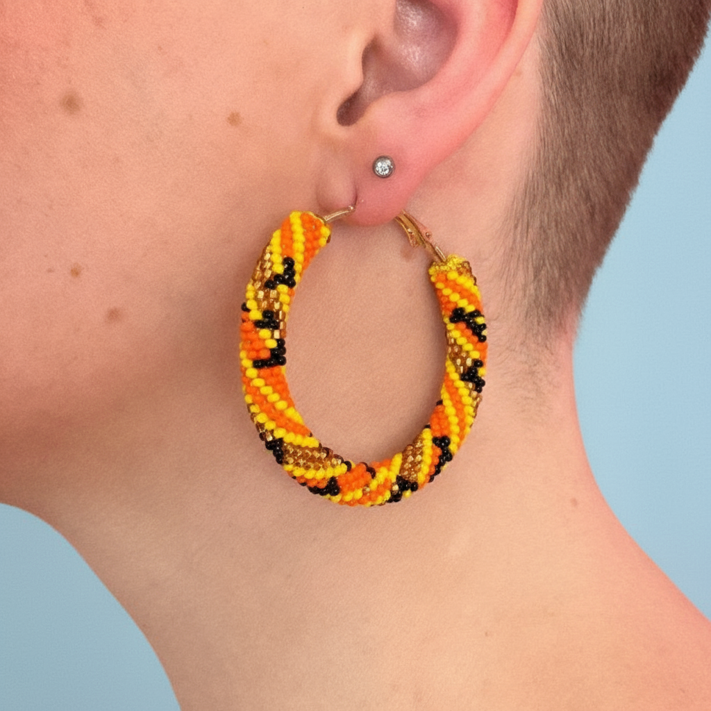 Close-up of an ear wearing a colorful hoop earring against a light blue background - Beadzy