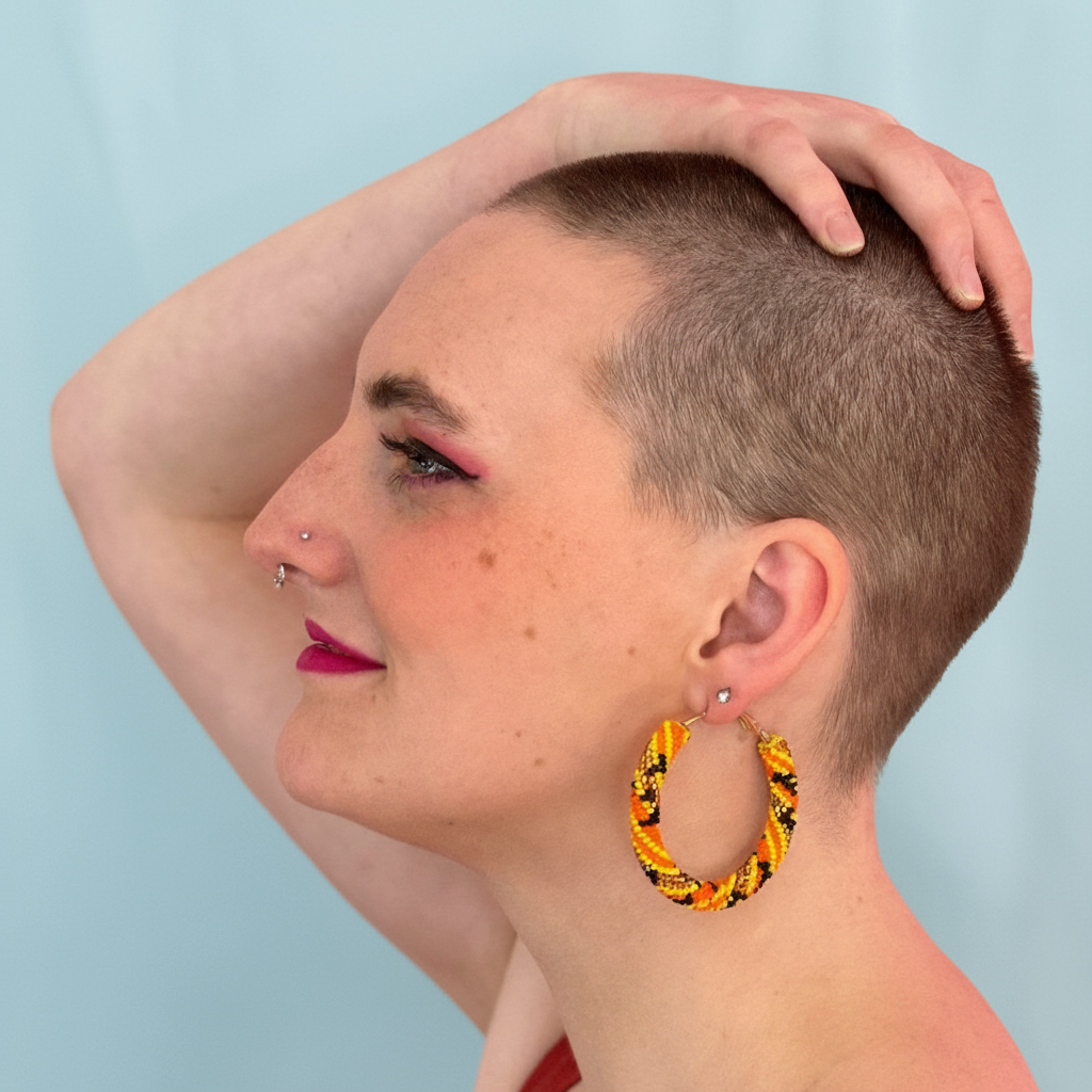 Woman with a shaved head wearing large hoop earrings against a light blue background - Beadzy