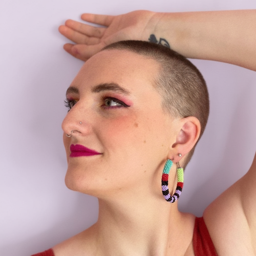 Person with a shaved head wearing colorful hoop earrings against a light purple  background - Beadzy