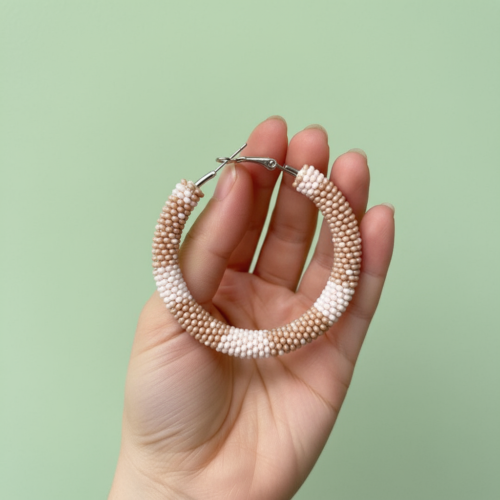 Hand holding a pair of beaded hoop earrings against a light green background - Beadzy