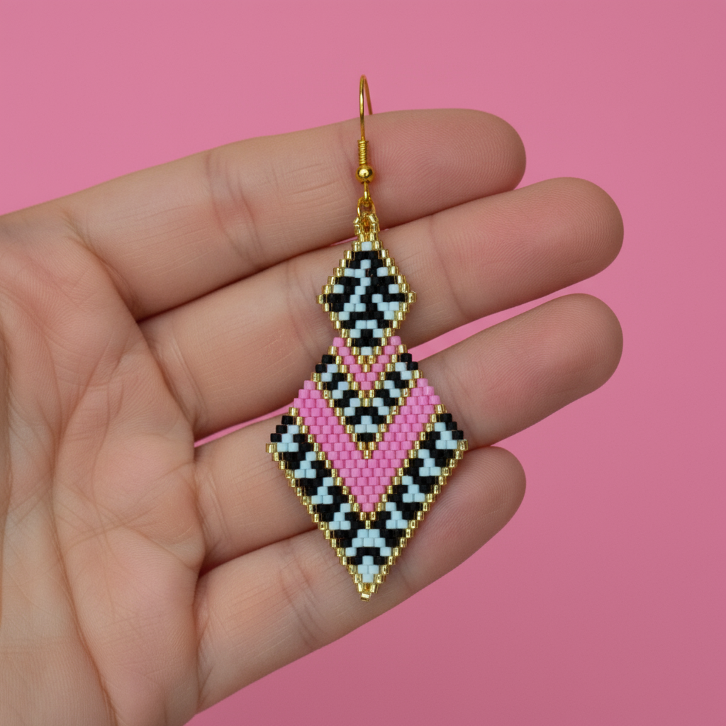 Beaded earrings held in a hand against a pink background - Beadzy