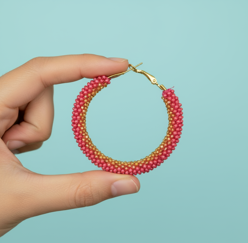 Hand holding a beaded hoop earring with pink and gold colors against a light blue background - Beadzy