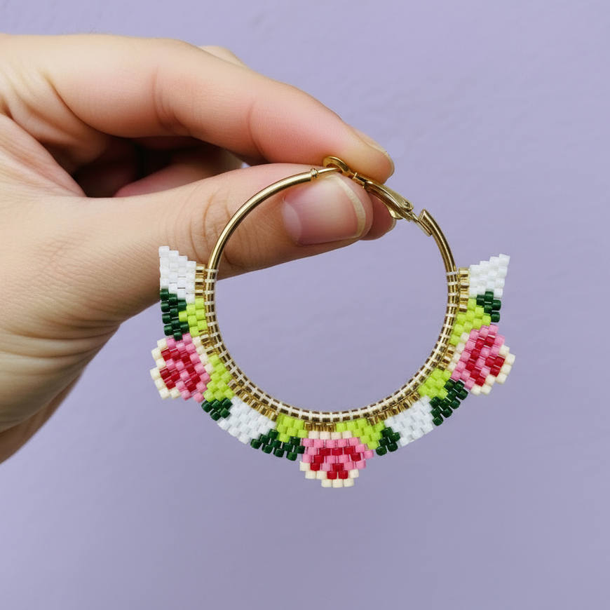 Hand holding a beaded hoop earring with floral design against a purple background- Beadzy