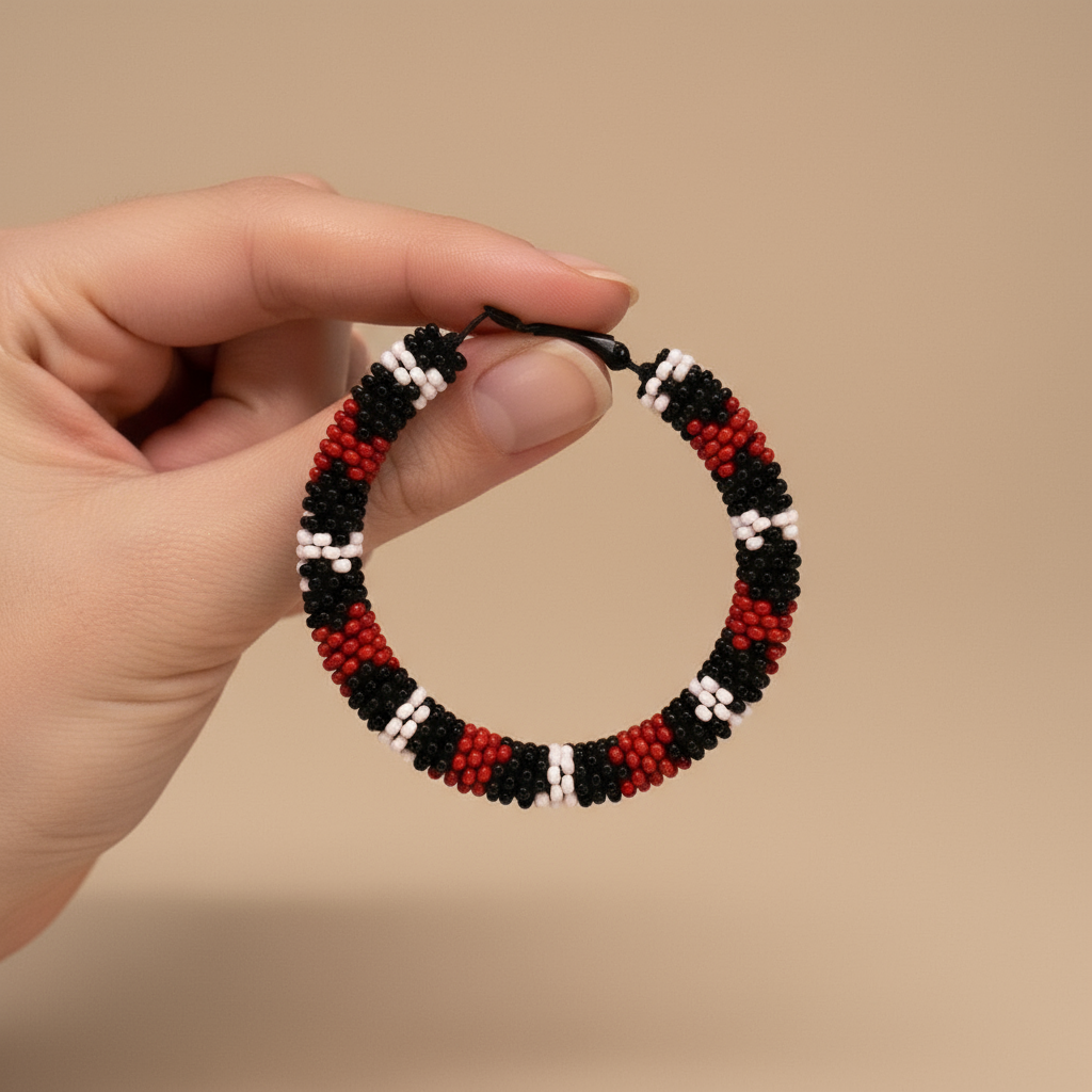 Hand holding a beaded hoop earring with red, black, and white pattern on a beige background - Beadzy