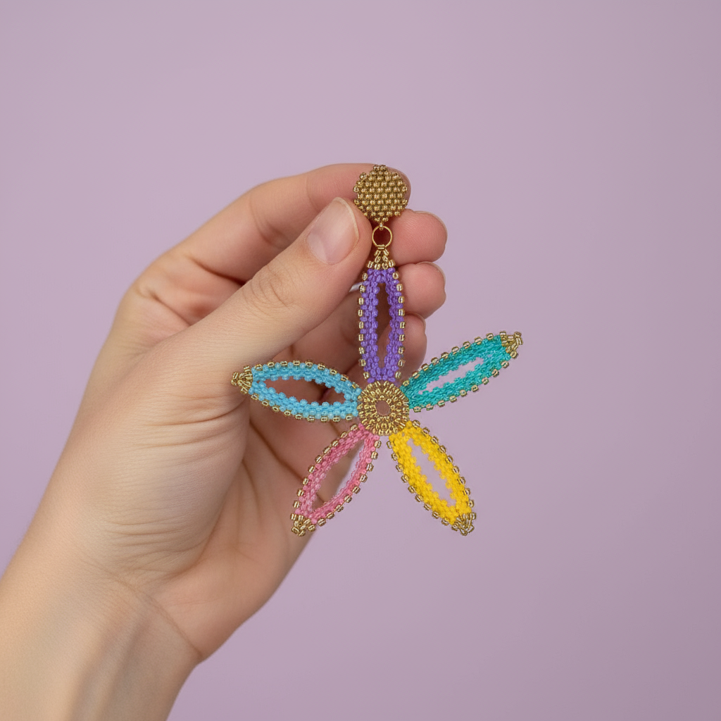 Hand holding a colorful beaded flower-shaped earring against a purple background - Beadzy