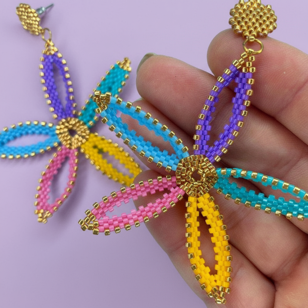 Colorful beaded flower earrings held by a hand on a light purple background - Beadzy