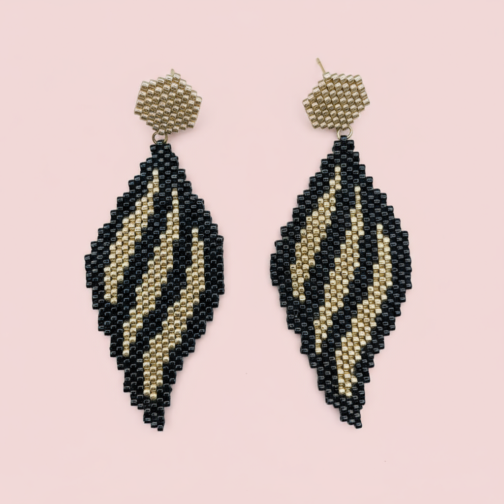 Pair of black and gold beaded earrings on a pink background - Beadzy