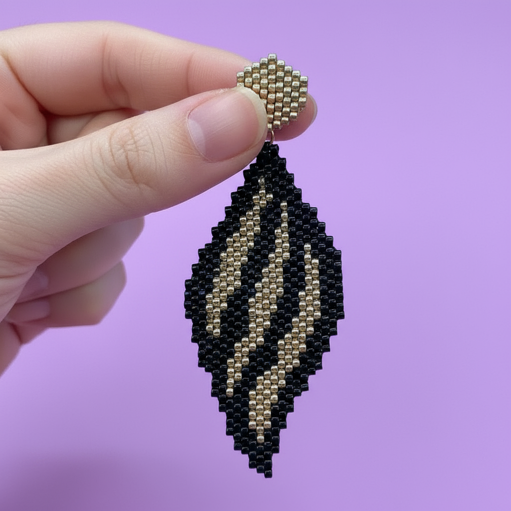 Hand holding a black and gold beaded earring against a purple background - Beadzy