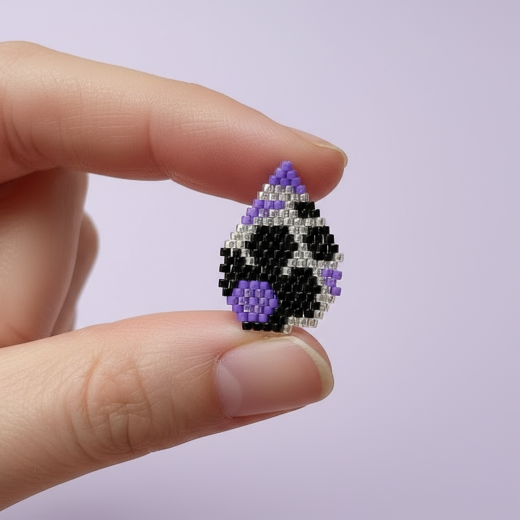 Hand holding a small beaded art piece with purple and black design on a pink background